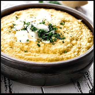 A warm bowl of smooth, creamy yellow polenta garnished with freshly shaved parmesan cheese and herbs